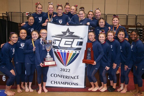 Penn gymnasts pose with the GEC Championship banner and their championship trophies.