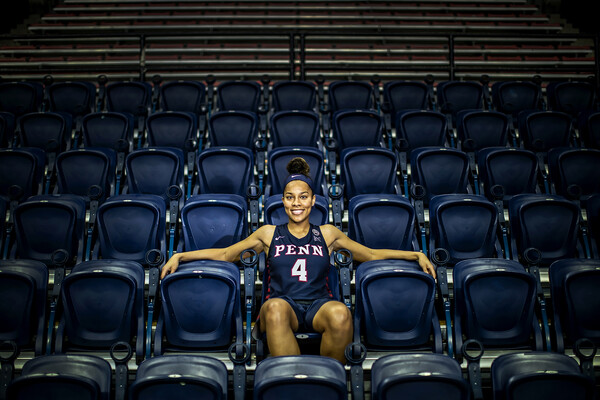 Wearing her Blue Penn jersey, Kennedy Suttle sits in the bleachers at the Palestra with her arms draped across the seats.