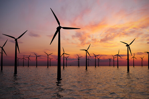 Wind turbines in water, with a sunset in the background. 