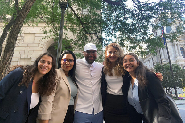 Five people stand in a group smiling outside. 