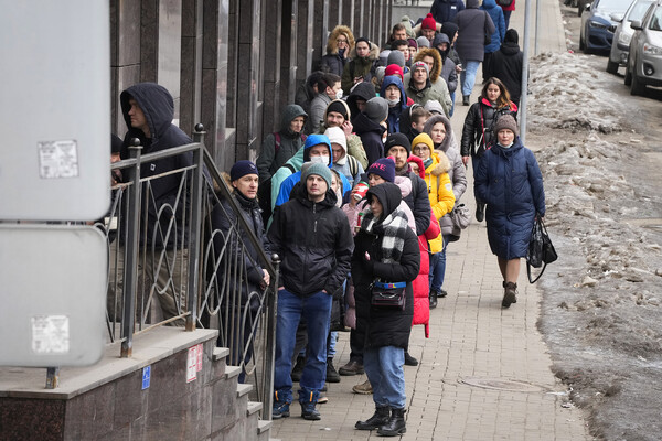 A line of people wearing winter coats and hats extends down a sidewalk in St. Petersburg, Russia, as they wait to use an ATM