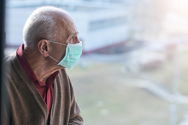 Elderly person sitting alone wearing a face mask.
