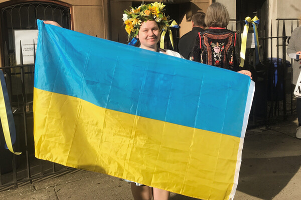 Alice Sukhina in Ukraine holding a large Ukrainian flag wearing a flower crown.