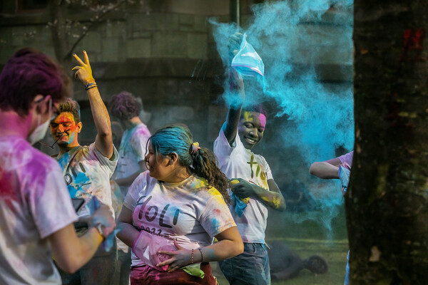 Students on College Green throw colorful powder in the air for Holi.