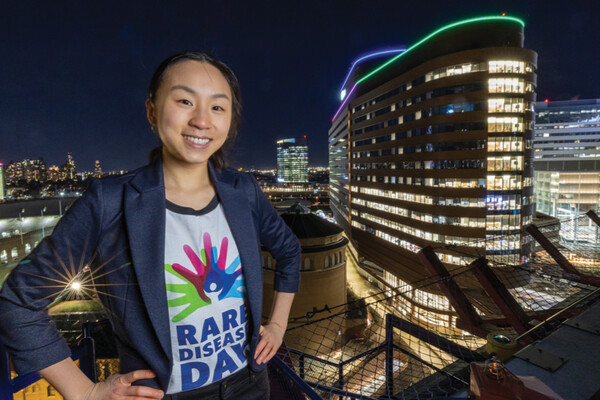 Magnolia Wang stands on an outdoor viewing point with HUP in the background illuminated in green and purple lights.