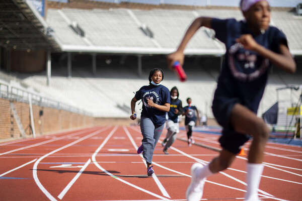 Middle school students run around a track, batons in hand