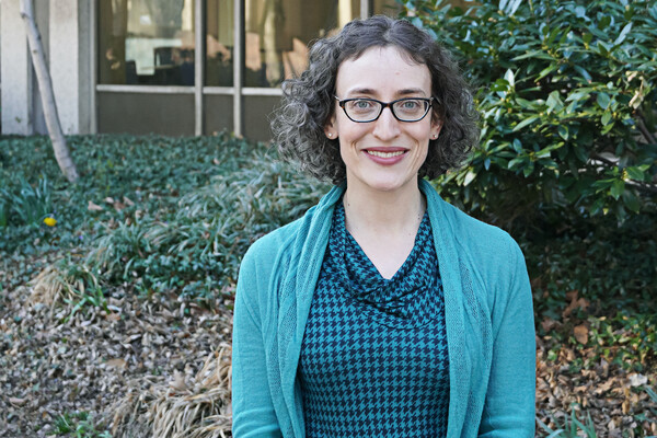 Rebecca Mendelson poses outside the library in front of green bushes