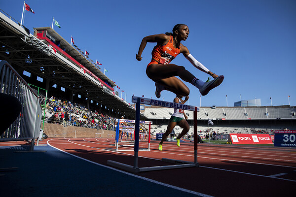 A runner jumps over a hurdle on a track.