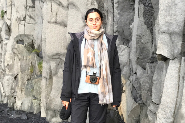 Eleanor Shemtov wearing a scarf and a camera around her neck standing in front of wall of rocks