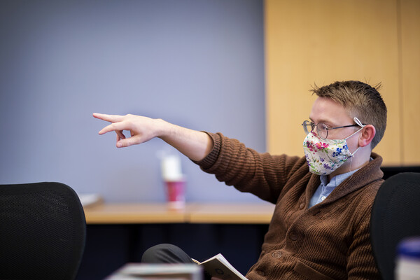 David Lydon-Staley sitting in a chair, pointing at the front of the room. 