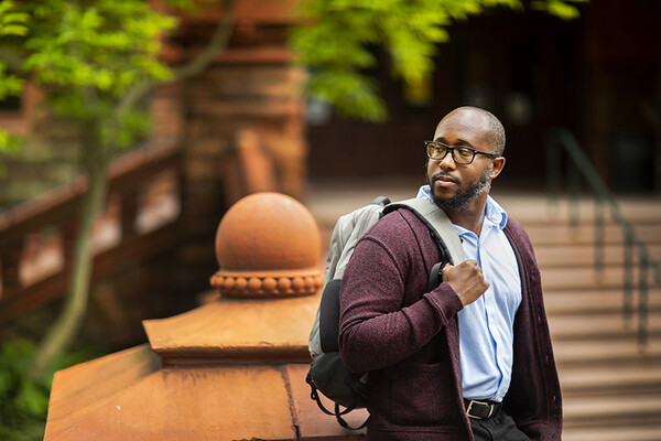 Jamaal Green wearing a backpack in front of the entrance to Fisher Fine Arts Library.