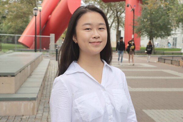 Angela Shen smiles in front of the red steel sculpture on Locust Walk