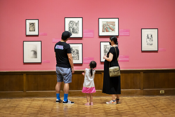 two adults and one child look at prints hanging on a very pink wall 