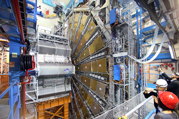 workers with hard hats stand next to the complex machinery of the Large Hadron Collider