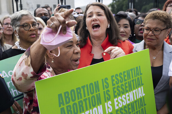 A crowd of people gathered, one holds a sign that reads ABORTION IS ESSENTIAL.