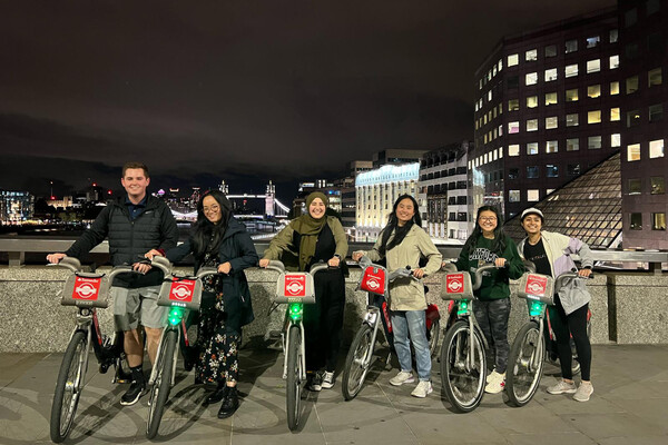 Six Wharton students riding bikes on a bridge at night.