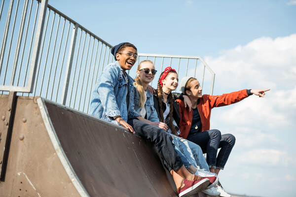Four adolescents sitting on the top of a skate ramp.