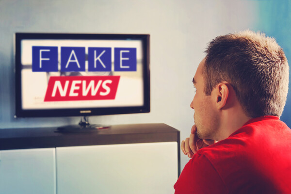 A person watching a television channel with the words FAKE NEWS on the screen.