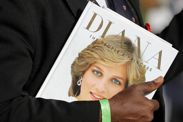 A book entitled "Diana, the People's Princess" with a photo of her face is being held by a man in a suit