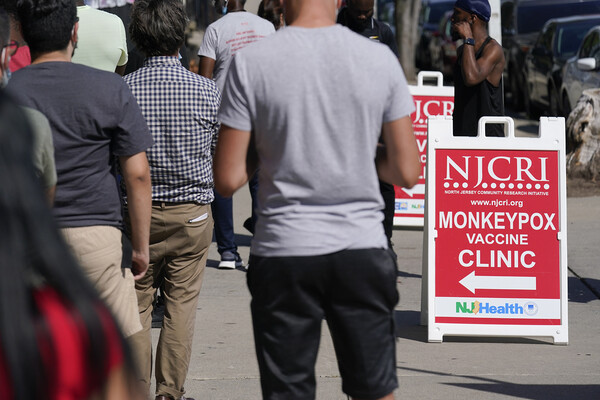 People lined up near a sign that says NJCRI Monkeypox Vaccine Clinic