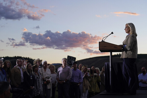 Liz Cheney speaks at a podium outside as sun sets