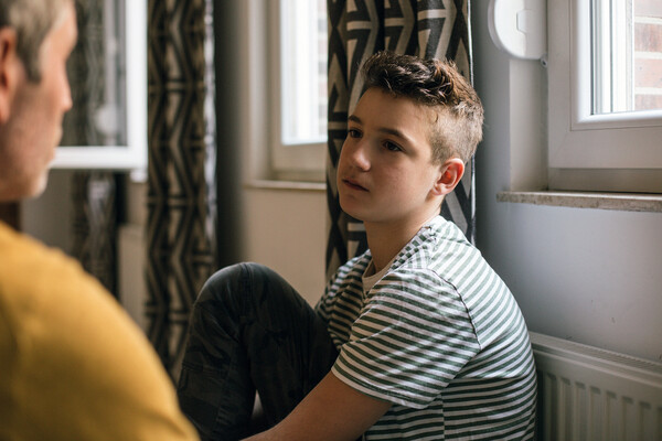 A young boy sitting on a couch listening to his parent.