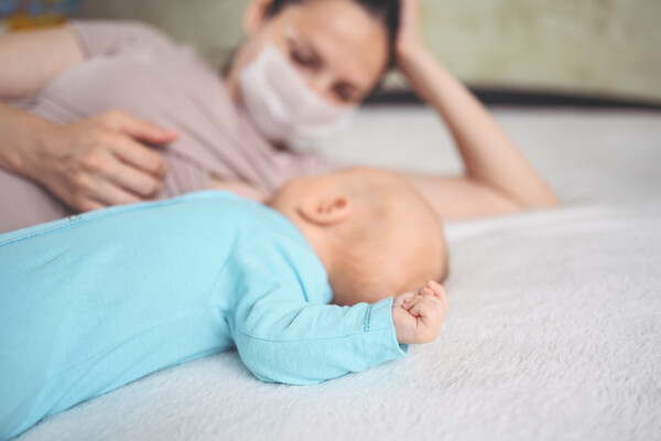 masked mother with baby on bed