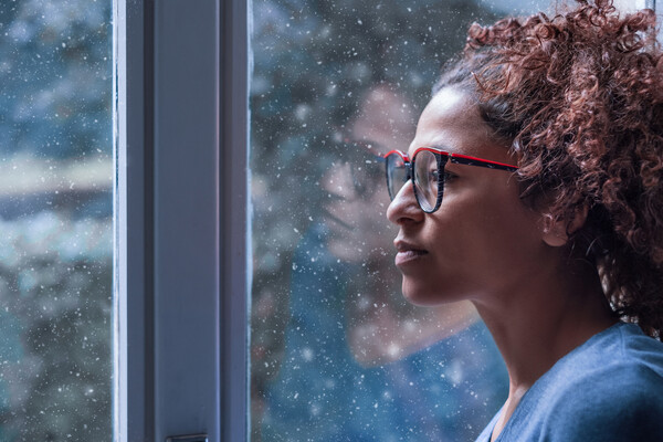 A depressed African American woman looks out a window.