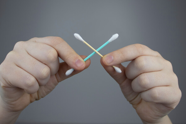 Two hands holding a cotton swab in an X formation.