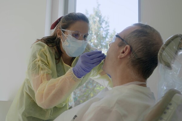 dental student in gown, gloves, and mask works on a patient in a dental chair