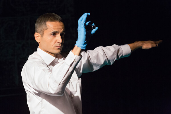 Ibrahim Miari performing on stage wearing a latex glove holding a small object.