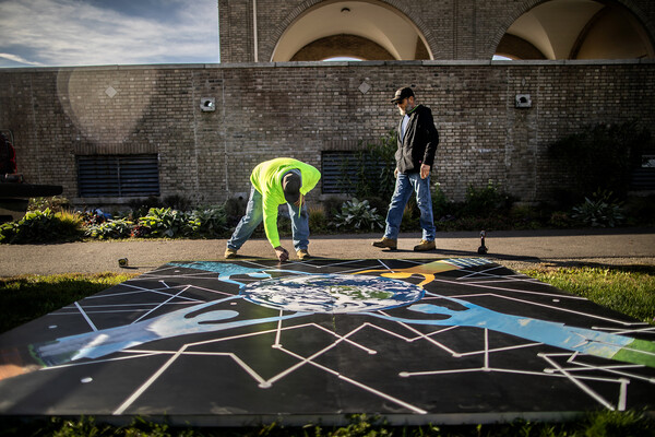 Two people standing over a large-scale painting that will be mounted on an outdoor portico.