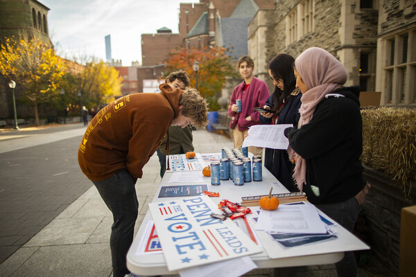 Students outside of Houston Hall at a table with drinks and signs for voting while another student looks at information on the table.