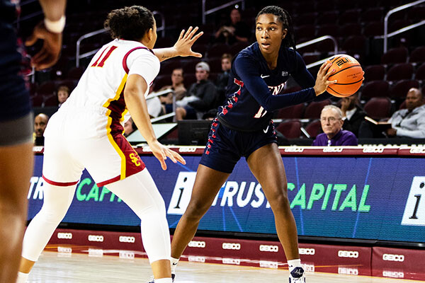 Simone Sawyer of the women's basketball team stands with the ball in a triple-threat position while being guarded by a defender.