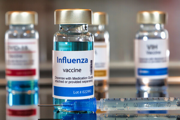 Four bottles of Influenza vaccine beside one medical syringe.