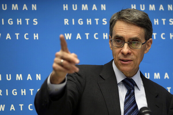 Kenneth Roth stands in front of a wall reading Human Rights Watch and points to the audience