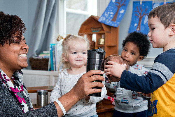 A caregiver "toasting" mugs with a toddler