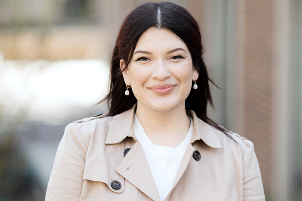 A woman in a trench coat smiles at the camera