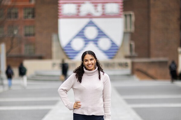 Student Anya Miller stands with her hand on her hip, smiling in front of the Penn shield at Penn Commons