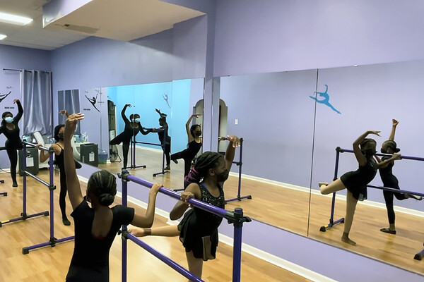 Young children practice ballet at a barre in a ballet studio.