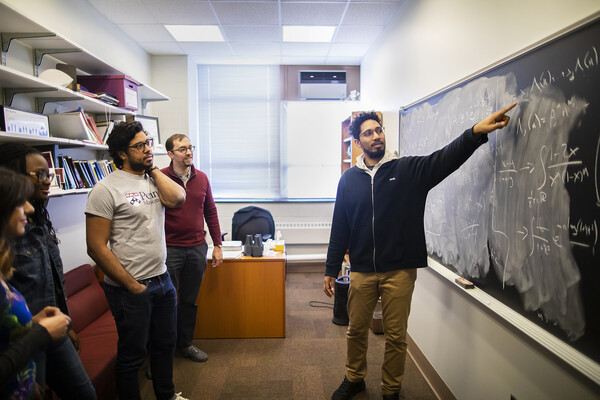 Four students and Philip Gressman, second from right, in a room looking at a chalkboard.