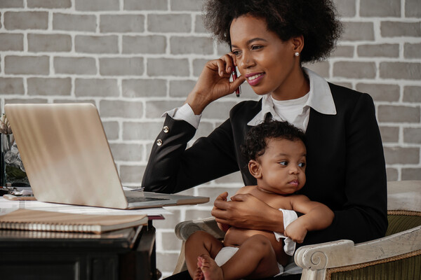 A parent working at a laptop with a small baby in their lap.