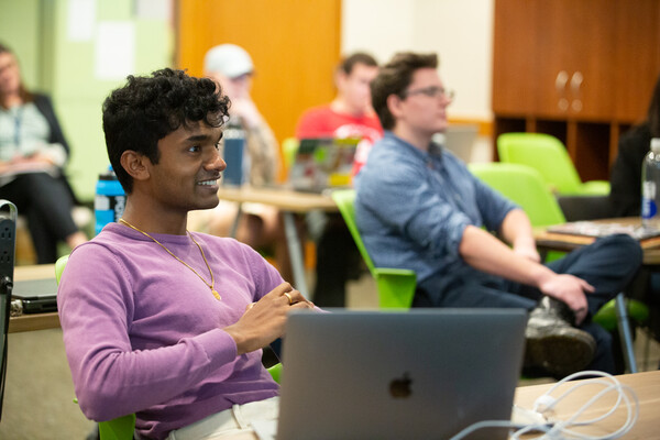 Alfie Arun smiles from behind his laptopas he listens to the student debate in the Future of Conservatism class.
