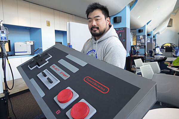 Tex Kang holds a giant replica of a gaming system control.