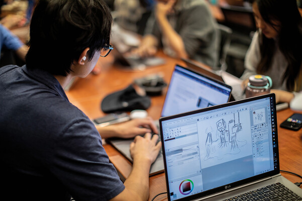 Students at a table with open laptops, one shows a draft of a video game.