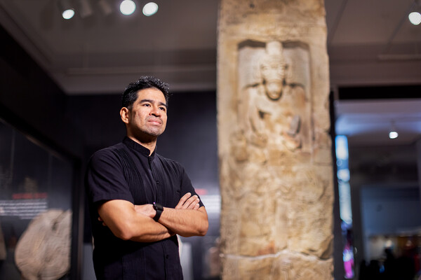 Francisco Diaz at the Penn Museum in front of a carved stone pillar