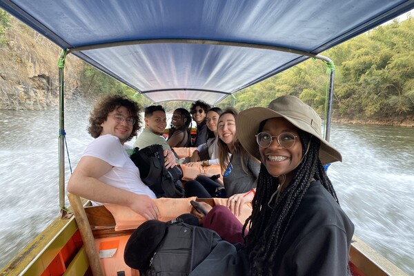 Seven students smile under the canopy of a motor-powered boat travelling on a river