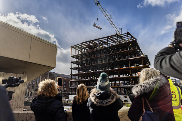 Onlookers watch as the last beam is put into place on a construction site.