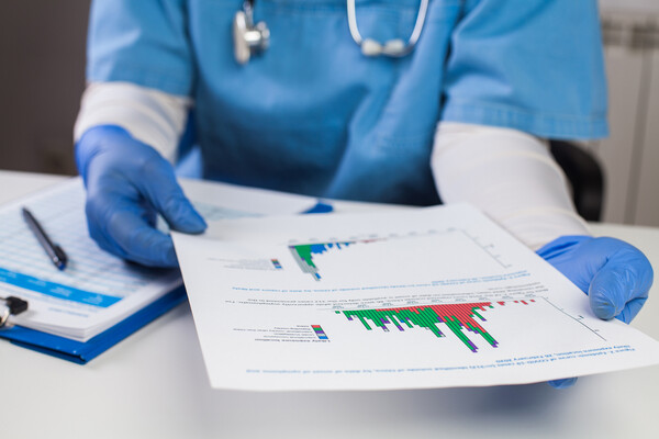 A medical professional wearing scrubs, latex gloves and a stethoscope looks at pages of graphs and data.