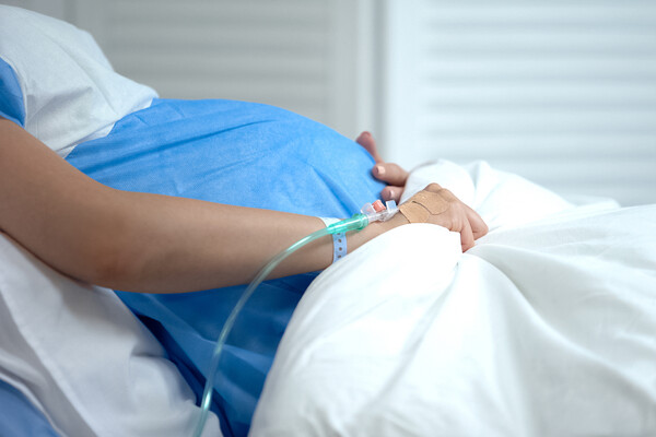 Pregnant person in hospital bed with IV drip in hand.